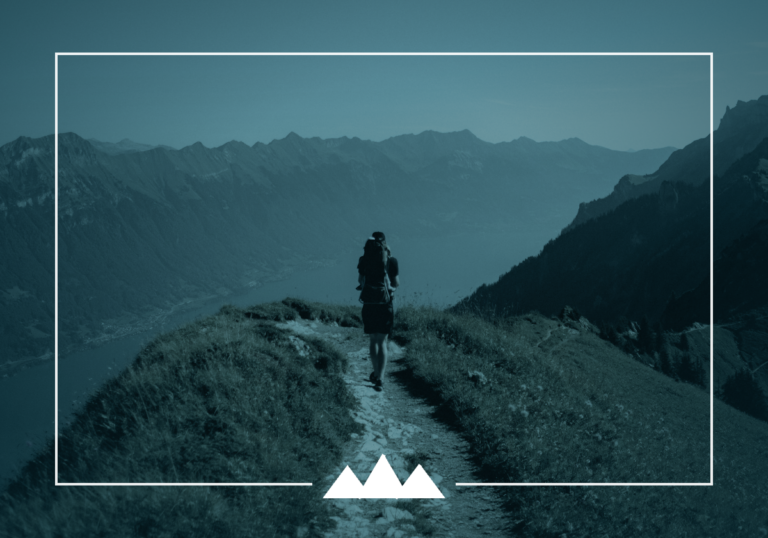 A lone hiker walks a narrow ridge trail toward distant mountains