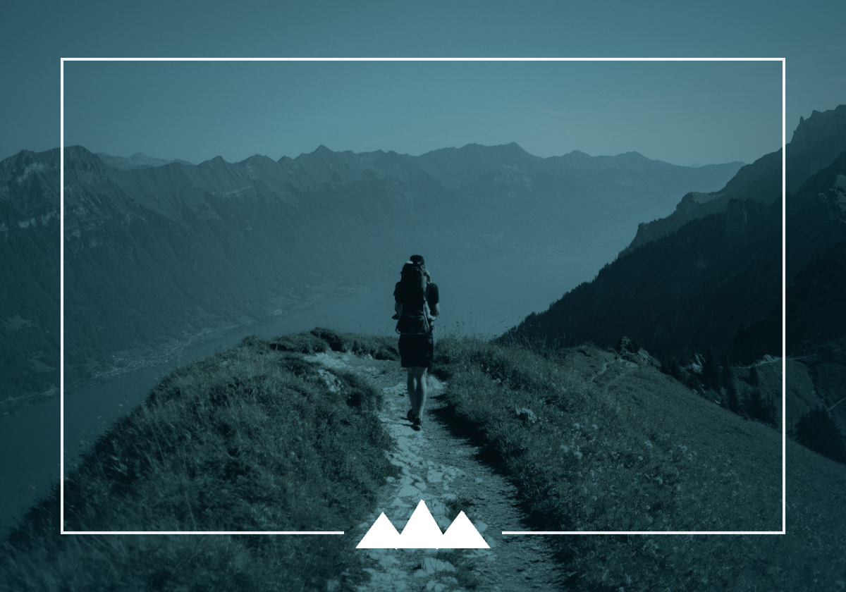 What a Successor Actually Inherits — featured A lone hiker walks a narrow ridge trail toward distant mountains